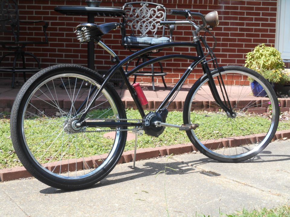 Black cruiser bicycle with red water bottle cage parked on sidewalk.