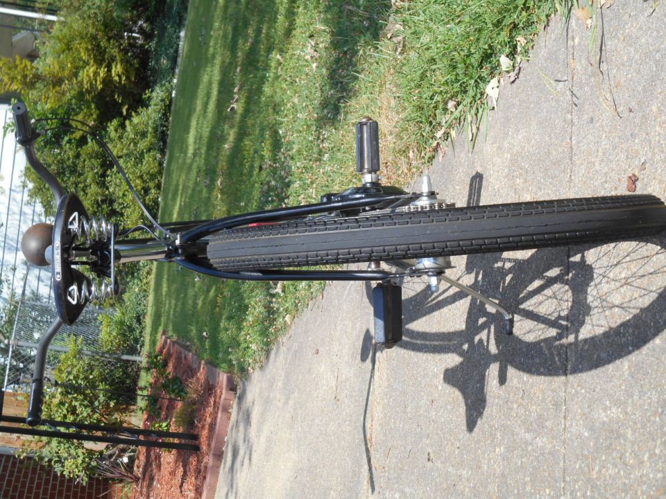 Black bicycle with sprung saddle and chain drive on concrete path.