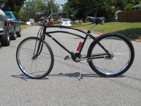 Black cruiser bicycle with red water bottle and kickstand on a road.