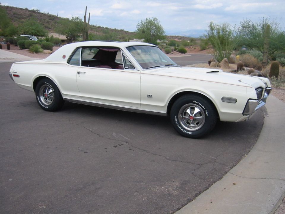 White 1968 Mercury Cougar parked on asphalt road with desert landscape.