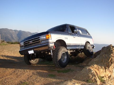 1989 Ford Bronco - This lifted 1987 Ford Bronco navigates a challenging rocky incline under a clear blue sky.