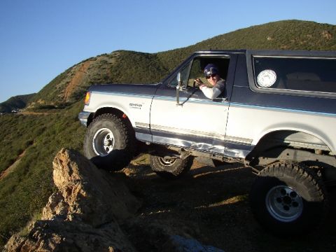 1989 Ford Bronco - 1989 Ford Bronco navigating a challenging rocky incline on a sunny day.