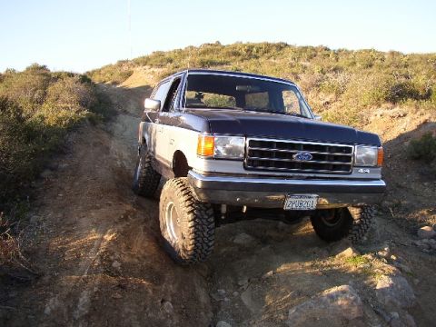 1989 Ford Bronco - Ford Bronco navigates a rocky, off-road trail with steep inclines and sparse vegetation.