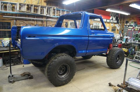 1979 Ford Bronco - A bright blue Ford Bronco body, likely undergoing restoration, is shown in a garage setting with various tools and equipment visible in the…