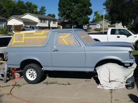 1988 Ford Bronco - A gray Ford Bronco is parked in a driveway, prepped for painting with masking tape and paper covering the windows and roof. A white pickup…