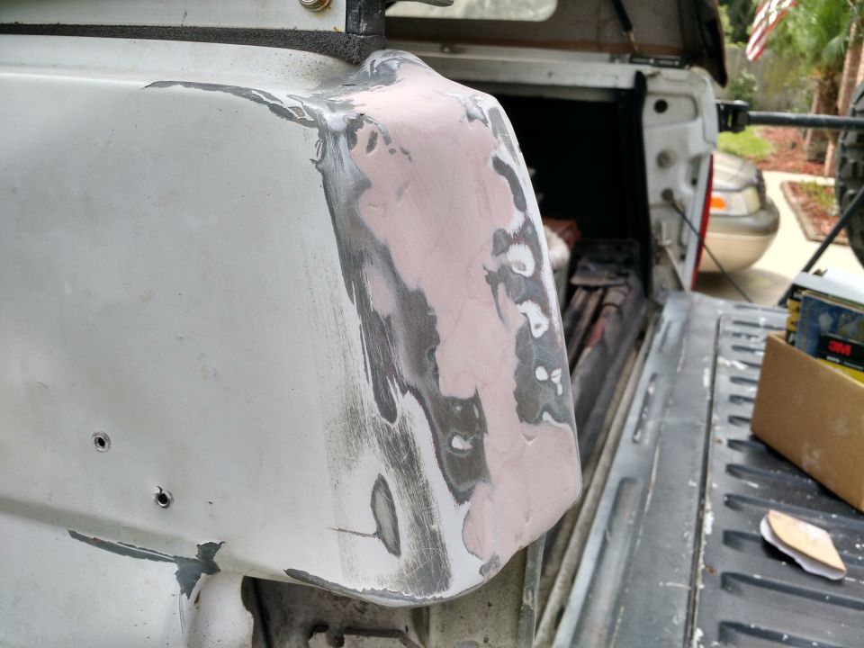 Close-up of truck bed corner with body filler and primer, showing repair work.