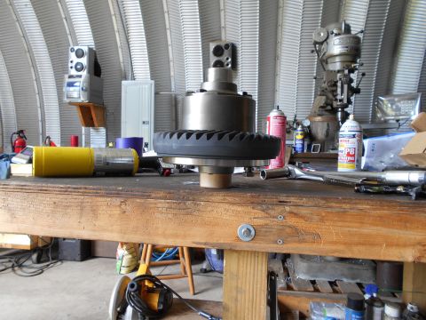 1992 Ford Bronco - A workbench in a garage setting with various tools and parts, including a large gear, spray cans, and a welding torch.