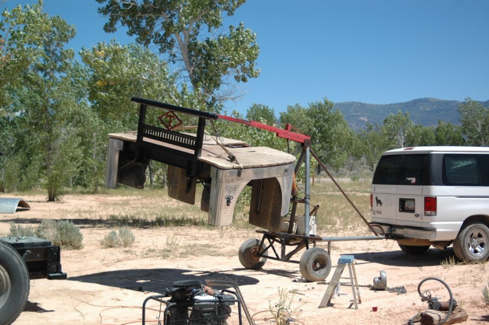 Custom trailer being lifted by a crane next to a white van.