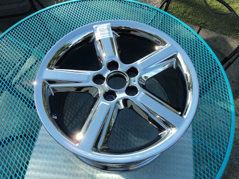 2004 Mercury Grand Marquis - A single, chrome five-spoke wheel is shown resting on a blue metal table. A white sticker with text is attached to the top spoke of the whe…
