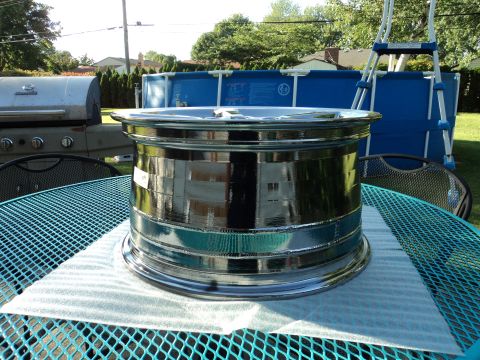 2004 Mercury Grand Marquis - A polished chrome wheel rim is displayed on a teal metal mesh table outdoors. In the background, a stainless steel grill and a blue above-g…