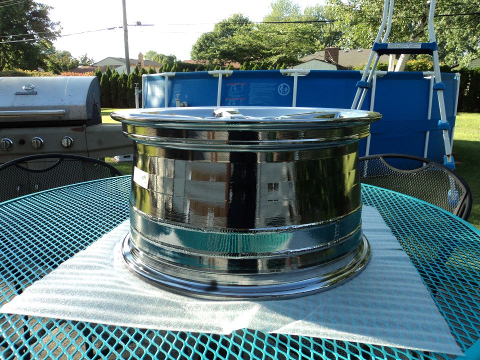 Polished chrome wheel rim on a teal table, with a grill and pool in the background.