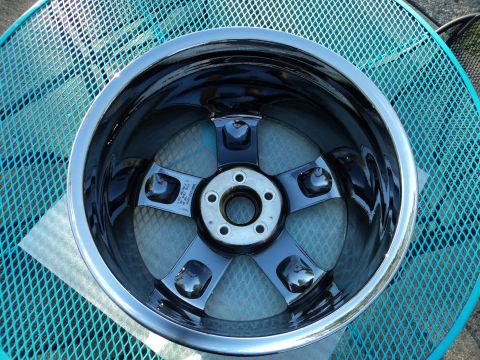 2004 Mercury Grand Marquis - A close-up, overhead view of a shiny black and chrome aftermarket wheel with a five-spoke design, resting on a blue mesh table.