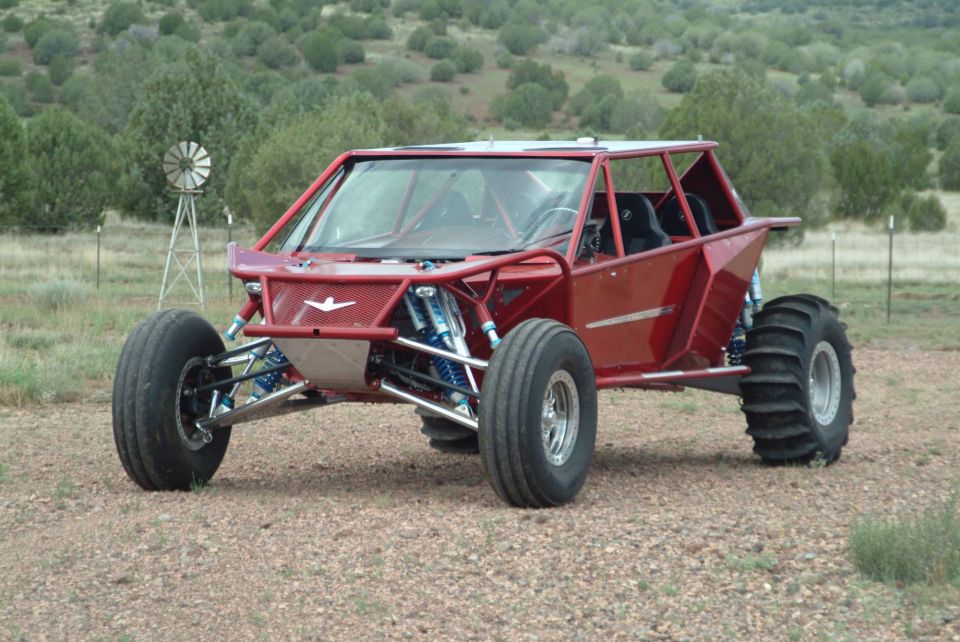 Custom red dune buggy with large tires and roll cage, parked outdoors.