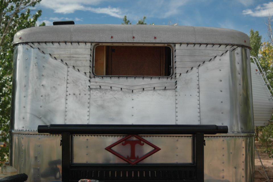 Rear view of an aluminum travel trailer with a window and decorative rivets.