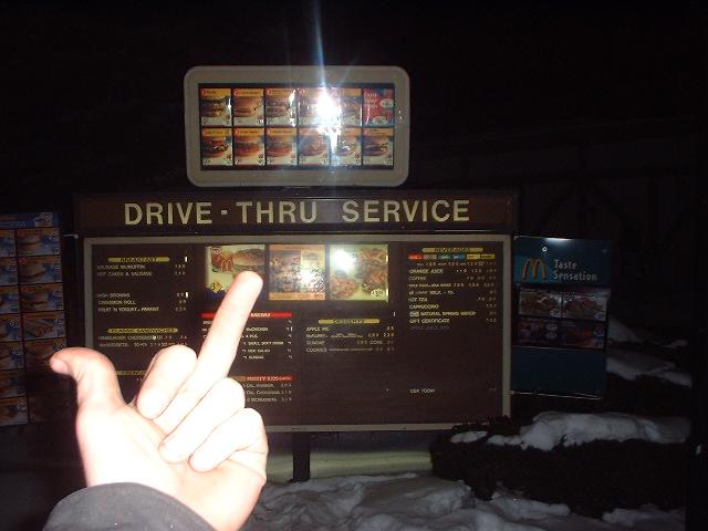 McDonald's drive-thru menu board at night with a hand gesture in foreground