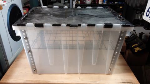 1985 Toyota 4Runner - A clear plastic storage bin with a black lid and metal reinforcements is shown on a wooden surface.