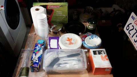 1985 Toyota 4Runner - A collection of camping kitchen supplies is laid out on a table, paper goods, cookware, and utensils.
