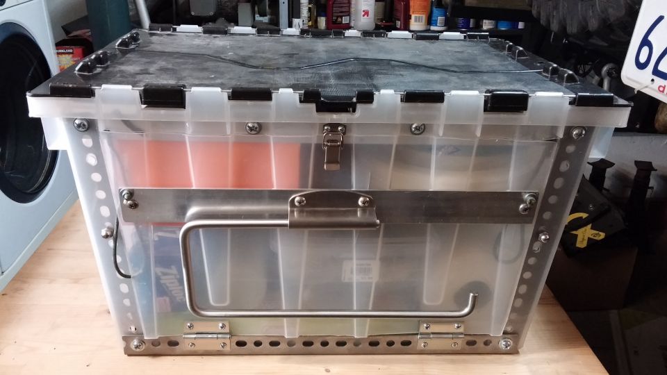 Clear plastic storage bin with metal banding and a folding handle, sitting on a wooden surface