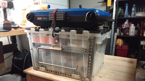 1985 Toyota 4Runner - Coleman camping stove sits atop a clear storage bin, with a drill visible on a workbench nearby.