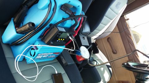 1985 Toyota 4Runner - A blue power inverter and charging equipment are set up inside a vehicle, powering a smartphone.