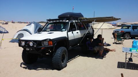 1985 Toyota 4Runner - A modified SUV is parked on the sand with camping gear, including tents and an awning, under a clear blue sky.