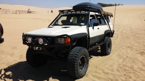 1985 Toyota 4Runner - A modified white Toyota 4Runner is seen on sand dunes, with another vehicle partially visible to the left.