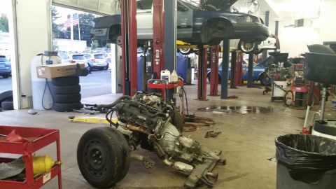 2001 Ford Crown Victoria - A garage scene with a disassembled car engine and chassis in the foreground and vehicles on lifts in the background.
