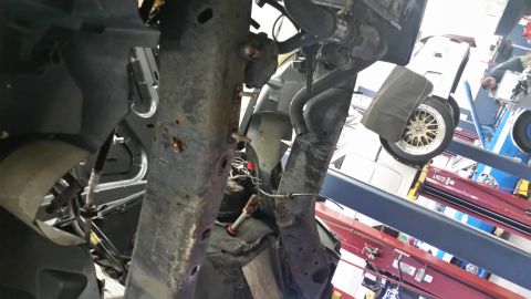 2001 Ford Crown Victoria - Close-up view of heavily rusted structural components and suspension parts, with a glimpse of a vehicle's wheel in the background.
