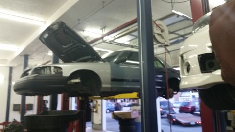 2001 Ford Crown Victoria - A two-tone Ford Crown Victoria is raised on a hydraulic lift in a repair shop with its hood open.