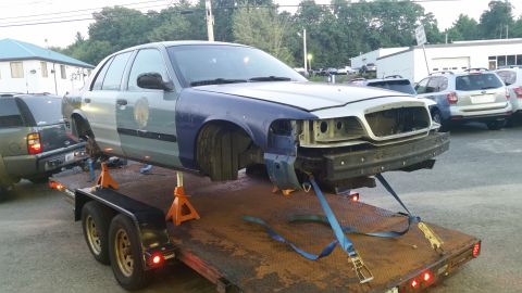 2001 Ford Crown Victoria - A Ford Crown Victoria is being transported on a trailer, with its front end disassembled.