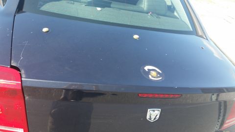 2001 Ford Crown Victoria - The rear of a dark sedan shows several bullet holes and a Dodge emblem on the trunk.