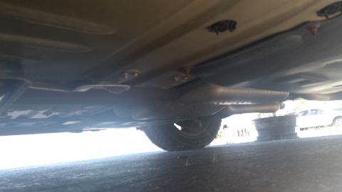 2001 Ford Crown Victoria - The underside of a car is visible, with exhaust pipes and a tire. Another vehicle is parked in the background.