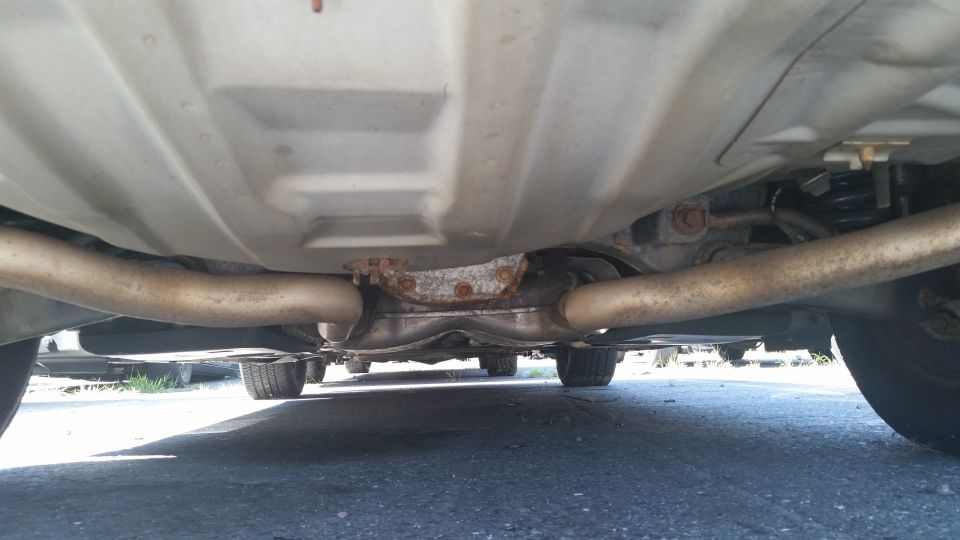 Underside view of a car's exhaust system and rear axle. Dual exhaust pipes are visible