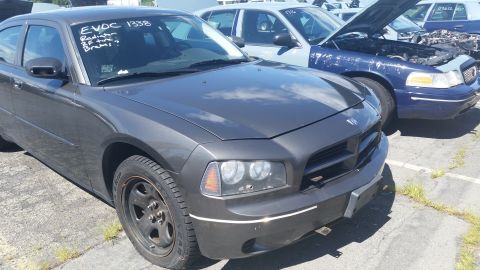 2001 Ford Crown Victoria - A dark gray Dodge Charger is parked in a lot next to a blue police car with its hood open.