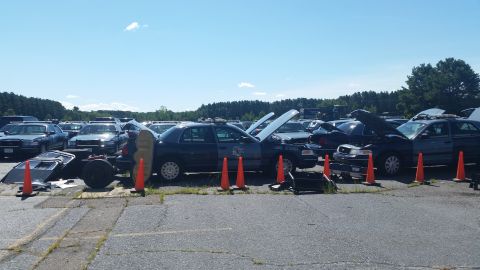 2001 Ford Crown Victoria - A collection of police vehicles, some appearing to be undergoing maintenance or dismantling, are parked outdoors under a clear sky.