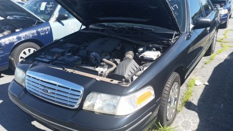2001 Ford Crown Victoria - A black 2001 Ford Crown Victoria is parked with its hood open, revealing the engine compartment.