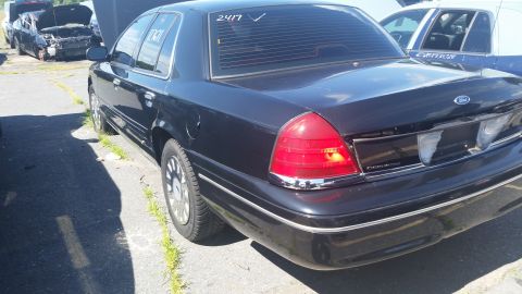 2001 Ford Crown Victoria - Rear view of a dark Ford Crown Victoria in a junkyard setting.