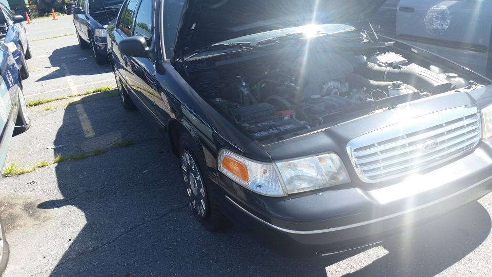 Black Ford Crown Victoria with hood open, parked in lot next to other cars