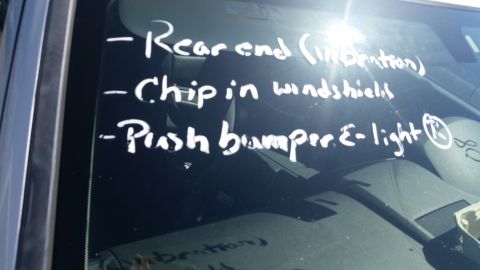 2001 Ford Crown Victoria - Photograph of a windshield with grease-pencil auction notes listing rear end, windshield chip, and push bumper, not a technical document.