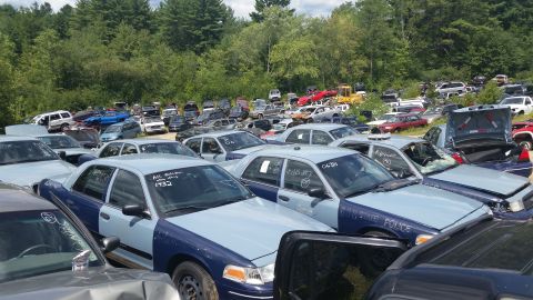 2001 Ford Crown Victoria - Photo of a salvage yard full of vehicles with a tow truck, not a document.