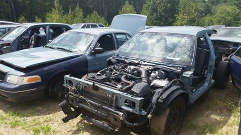 2001 Ford Crown Victoria - Photo of a partly dismantled sedan with exposed engine in a salvage yard, not a document.