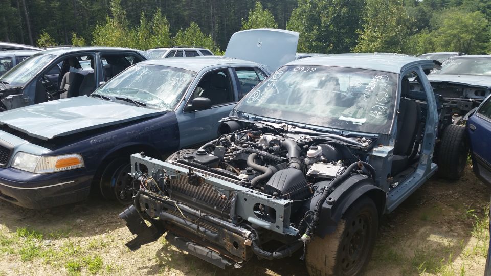 Stripped sedan with engine and front subframe exposed in a salvage yard