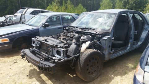 2001 Ford Crown Victoria - Photo of a dismantled sedan with exposed engine and chassis in a yard, not a document.