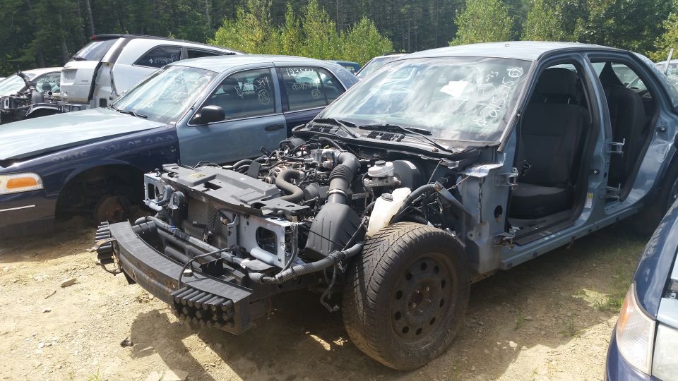 Sedan stripped of front bodywork showing engine and chassis in a salvage yard