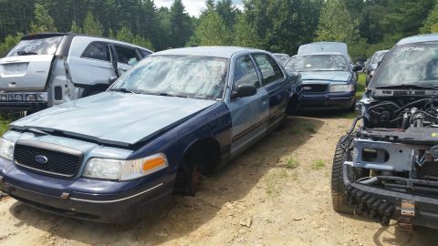 2001 Ford Crown Victoria - Photograph of several Ford Crown Victoria sedans parked in a junkyard, not a technical document.