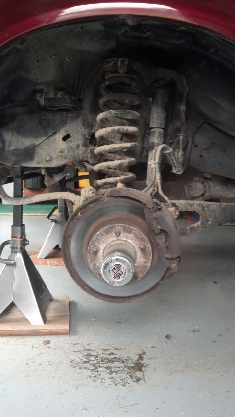 1996 Ford Bronco - A close-up view of the front suspension and brake assembly of a vehicle, likely a 1996 Ford Bronco, supported by jack stands. The vehicle i…