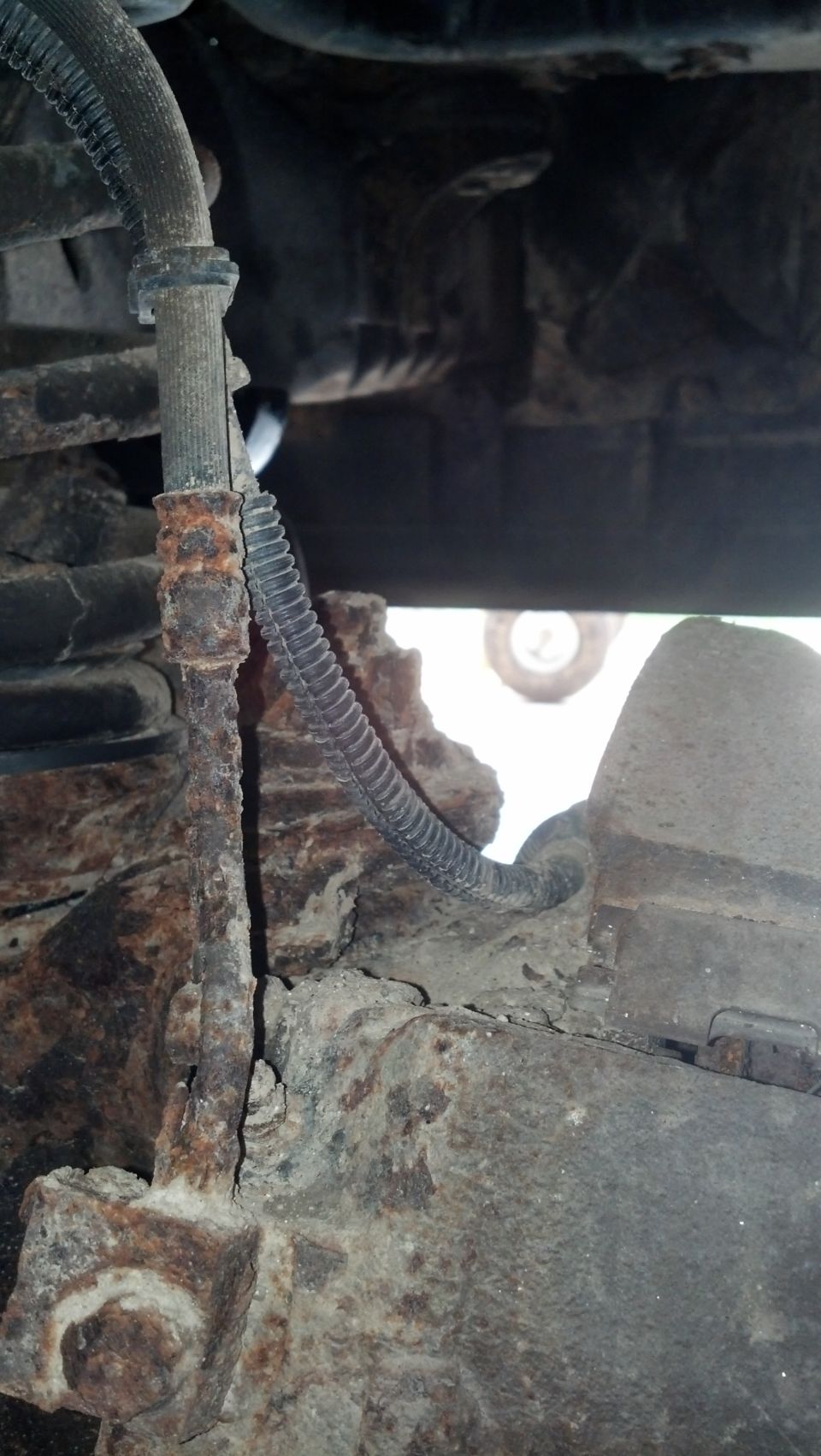 Heavily rusted brake line and suspension components on a vehicle underside.