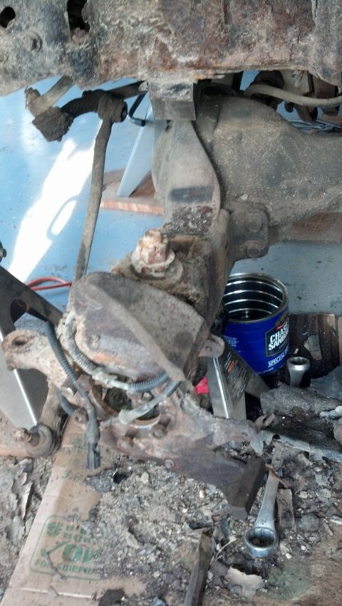 1996 Ford Bronco - A heavily rusted suspension component of a vehicle is shown, possibly from a 1996 Ford Bronco, supported by a jack stand. A blue can with '…