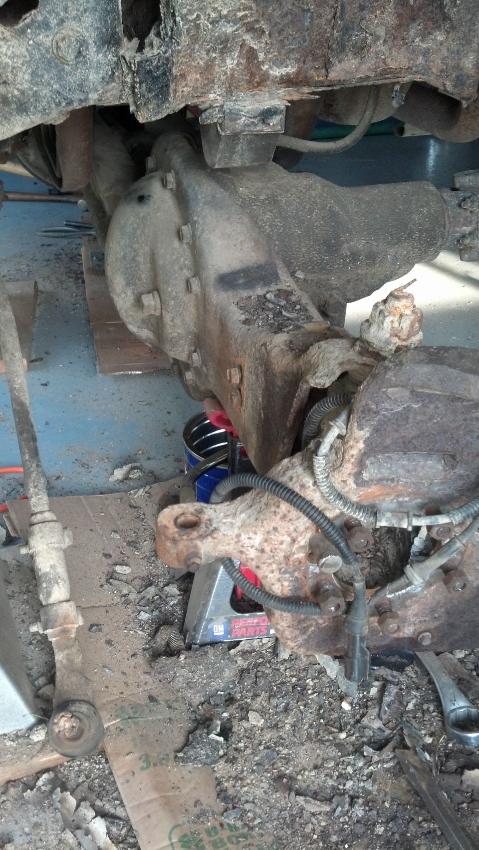 Heavily rusted vehicle front differential and suspension parts on a jack stand.
