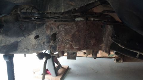 1996 Ford Bronco - The underside of a vehicle shows significant rust and corrosion on the frame and suspension components. The vehicle is supported by jack st…
